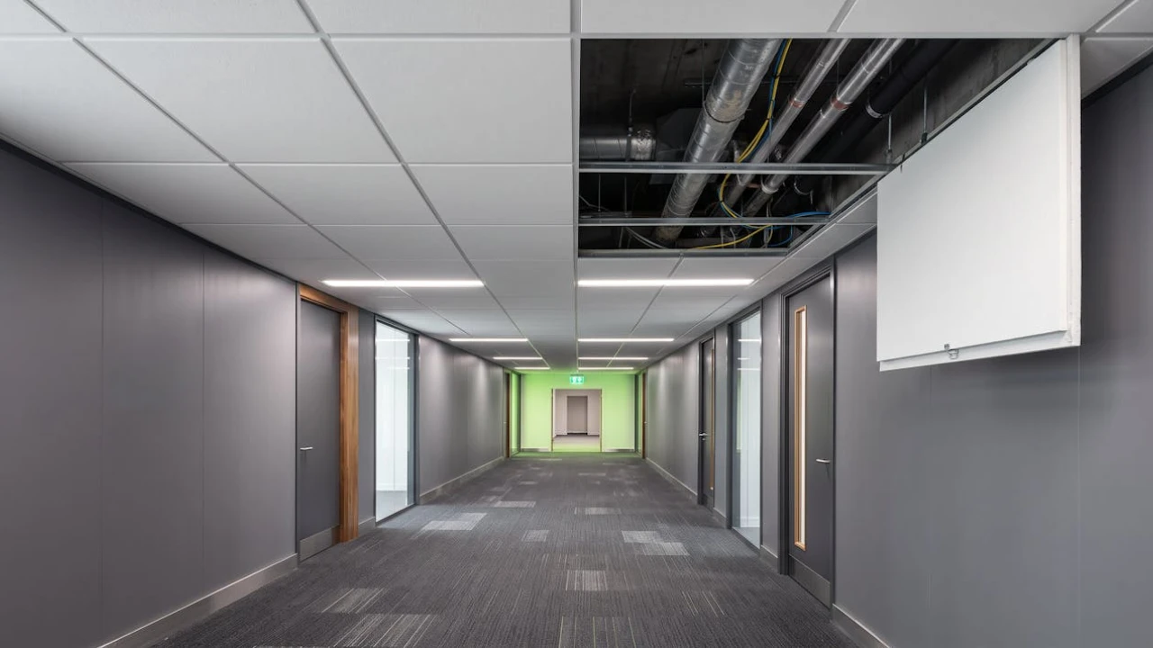 Suspended ceiling tile lifted in a commercial office corridor revealing services in the void above
