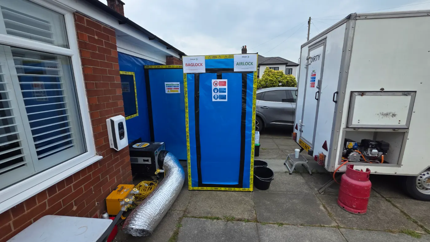 Sealed asbestos enclosure with airlock and baglock beside a decontamination unit on a residential driveway